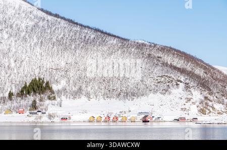 Eine malerische Winterszene eines norwegischen Fjords mit farbenfrohen Häusern an einem verschneiten Berghang, die sich in den ruhigen Gewässern darunter spiegeln Stockfoto