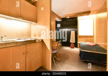 Ein kompaktes, modernes Studio mit hellen Holzschränken und -Oberflächen, einem kleinen Küchenbereich, einem Arbeitsbereich und einem gemütlichen Schlafbereich. Minimalistisches Dekor Stockfoto