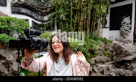 Eine Frau nimmt im Yuyuan-Garten in Shanghai, China, auf, umgeben von üppigem Grün und traditioneller Architektur, während sie mit ihrer Kamera interagiert. Stockfoto