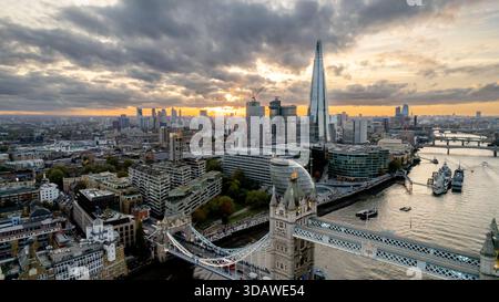 Fesselnde Luftaufnahme von Londons Tower Bridge, mit dem berühmten Shard im Hintergrund, während eines atemberaubenden Sonnenuntergangs. Die Themse schlängelt sich durch den Fluss Stockfoto