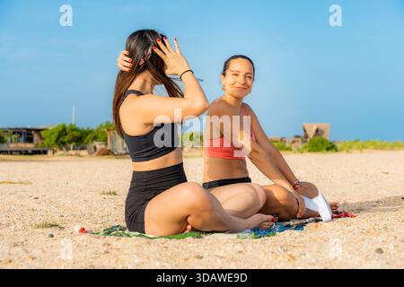 Junge Frauen üben Yoga an einem malerischen Strand in Kolumbien, genießen einen sonnigen Tag und den ruhigen Blick auf das Meer, fördern Wellness und Achtsamkeit durch Stockfoto
