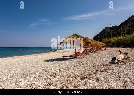 Ein leerer Strand in Lefkada, Griechenland, mit Strohschirmen und Liegestühlen unter hellem, sonnigem Himmel. Die friedliche mediterrane Umgebung ist ein Highlight Stockfoto