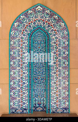 Der Blick auf eine reich verzierte, bogenförmige Nische mit aufwendigen blau-weißen Blumenfliesen, die sich an einer schlichten Wand befinden, schafft einen markanten Kontrast, Muscat, Muscat Go Stockfoto