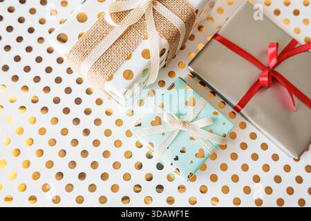 Flache Anordnung von verschiedenen Geschenkboxen mit stilvoller Verpackung und Bändern auf goldenem Polka Dot Hintergrund. Helle, festliche und elegante Komposition für Celebra Stockfoto