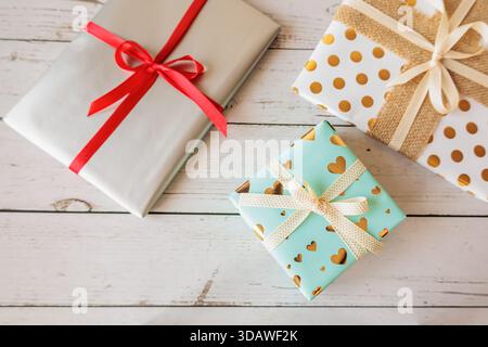 Blick von oben auf wunderschön gewickelte Geschenke mit Bändern auf rustikalem weißem Holzhintergrund. Gemütliche, festliche Wohnung für Feiertage, Geburtstage oder romantische Okka Stockfoto
