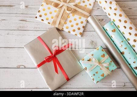 Geschenkverpackungsset mit Geschenken und Rollen dekorativen Papiers auf rustikalem Holzhintergrund. Flache Liege für Feiertage, Basteln und festliche Vorbereitungen. Br Stockfoto
