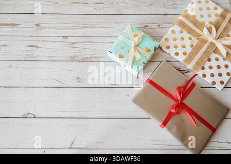 Drei farbenfrohe Geschenke mit strukturierter und dekorativer Verpackung auf einem hellen Holztisch. Rustikale und fröhliche flache Lage ideal für Weihnachten, Valentinstag Stockfoto