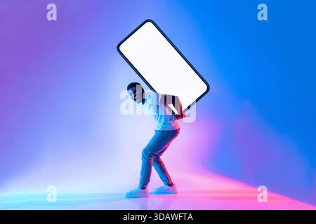 Mann lächelt, während er einen großen leeren Bildschirm in einer bunten Beleuchtung hält Stockfoto