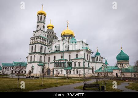 Der Blick auf eine große weiße Kathedrale mit markanten goldenen und grünen Kuppeln erhebt sich majestätisch vor einem grauen Himmel, eingerahmt von grünen Rasenflächen, Istra, Moskowskaja Stockfoto