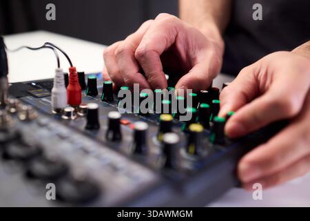 Tastfinger bedienen die beleuchteten Drehregler während der Soundcheck-Einrichtung, professionelle Techniker stellen die Soundausrüstung mit mehreren angeschlossenen Kabeln fertig Stockfoto