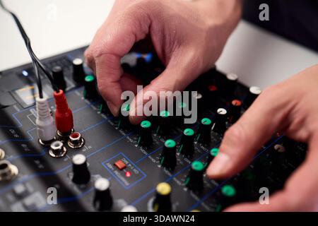Tastfinger bedienen die beleuchteten Drehregler während der Soundcheck-Einrichtung, professionelle Techniker stellen die Soundausrüstung mit mehreren angeschlossenen Kabeln fertig Stockfoto