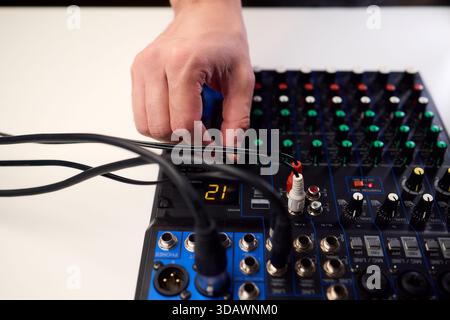Tastfinger bedienen die beleuchteten Drehregler während der Soundcheck-Einrichtung, professionelle Techniker stellen die Soundausrüstung mit mehreren angeschlossenen Kabeln fertig Stockfoto