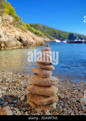 Ein Turm aus glatten Steinen an einem Strand in der Nähe von klarem Wasser Stockfoto