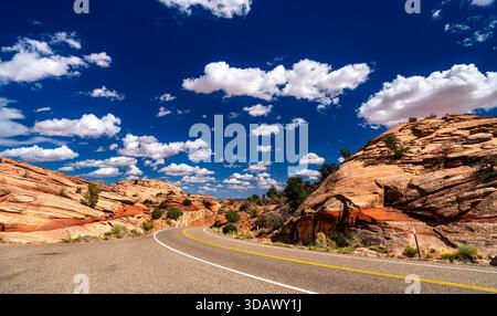 Der malerische Byway 12 schlängelt sich durch rote Sandsteinformationen im Grand Staircase-Escalante National Monument, Utah. Gepflasterte Autobahnkurven unter blauem Himmel mit weißen Wolken Stockfoto