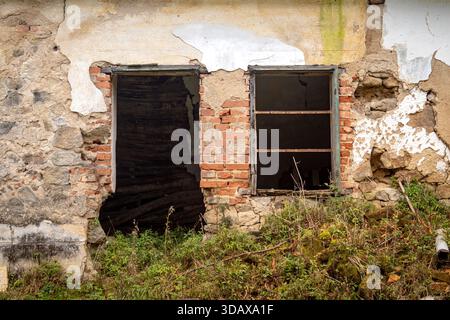 Blick aus der Nähe auf beschädigte Fenster und zerbröckelnde Ziegelsteine an der Fassade eines verlassenen Landhauses Stockfoto