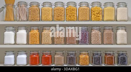Ein Regal voller Gläser mit verschiedenen Gewürzen und Körnern. Die Gläser sind in Reihen angeordnet, wobei einige Gläser mehr Gewürze enthalten als andere. Sce Stockfoto