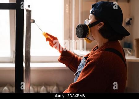 Side View-Frau in Atemschutzgerät mit Pinselfarbe Metall Tischgestell Möbelrestauration Projekt Stockfoto