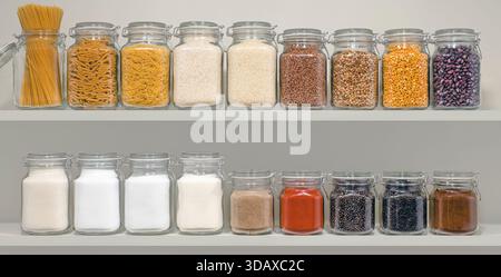 Ein Regal mit vielen Gläsern mit Lebensmitteln, einschließlich Nudeln, Zucker, Salz und Gewürzen. Die Gläser sind in Reihen angeordnet, wobei einige Gläser auf der linken und andere auf der liegen Stockfoto