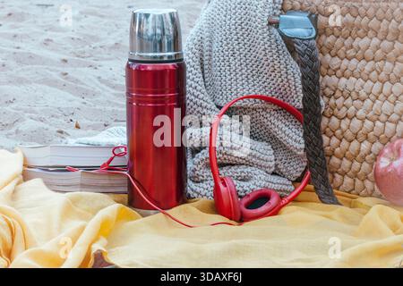 Sammeln Sie wichtige Gegenstände für einen entspannenden Tag im Freien, darunter Thermoskanne, Bücher, Kopfhörer, eine gemütliche Strickdecke und eine Strohtasche auf einem lebhaften YE Stockfoto