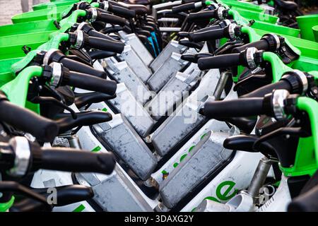 Eine Reihe geparkter Elektroroller mit grünem Lenker und silbernem Gehäuse, einsatzbereit. Stockfoto