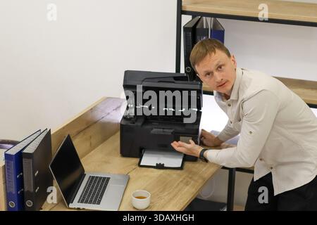 Verwirrte Büromitarbeiter zeigen, dass der Drucker ohne Papier geöffnet ist und in einem modernen Büro mit technischen Gadgets herumsteht. Stockfoto