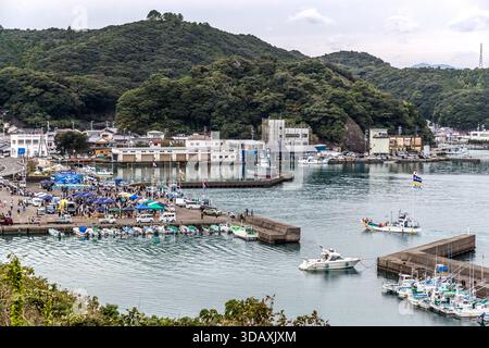 Ein geschäftiger Markt säumt den Hafen von Taiji, Präfektur Wakayama, Japan. Blaue Zeltdächer und japanische Flaggen kennzeichnen die Stände, Boote legen an den Piers an. Stockfoto