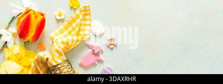 Helle Frühlingsblumen umgeben einen wunderschön gedeckten Tisch mit pastellfarbenen Ostereiern, Süßigkeiten und dekorativen Elementen, die den Geist der Urlaubsatmosphäre, Banner, einfangen Stockfoto