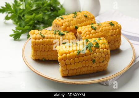 Stücke gekochter Maiskolben mit Petersilie auf weißem Marmortisch, Nahaufnahme Stockfoto