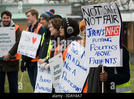 Am 26. April 2016 bildeten Ärzte des Queen Elizabeth Hospital in King's Lynn, Norfolk, am ersten Tag ihres beispiellosen All-Out-Streiks Streikposten – der erste in der Geschichte des NHS, der die Notversorgung entzog. Sie protestierten gegen den von Gesundheitsminister Jeremy Hunt auferlegten neuen Vertrag, der Wochenendprämien reduzierte, die „normalen“ Stunden verlängerte und als unterbewertete Ärzte angesehen wurde, während sie Patienten bei der Verfolgung eines siebentägigen NHS gefährdeten. Auf Schildern werden Botschaften wie „Hunt Must Go“ und „Safe Staffing rettet Leben“ angezeigt. Trotz Kontroversen fand die Aktion breite Unterstützung der Öffentlichkeit. Stockfoto