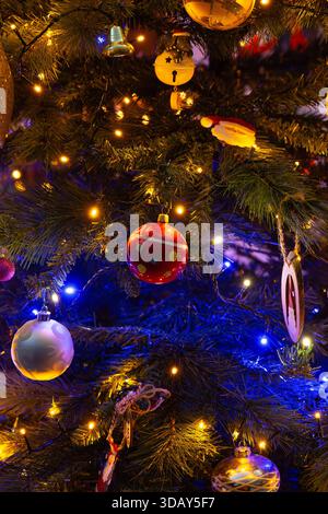 Üppige Komposition von mehrfarbigen Weihnachtsschmuck, die zwischen beleuchteten immergrünen Zweigen aufgehängt sind, sorgen für ein spektakuläres visuelles Festmahl an Feiertagen. Rot Stockfoto