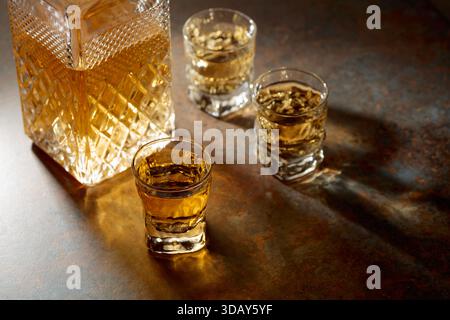 Karaffe und kleine Gläser Whiskey. Selektiver Fokus, lange und schöne Schatten auf einem Vintage-Hintergrund. Kopierbereich. Stockfoto