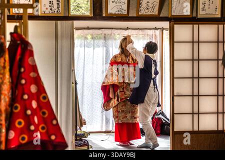 Ein Verkäufer hilft einem Kunden dabei, einen gemieteten Kimono im Heian-Stil in Nachi-Katsuura, Präfektur Wakayama, Japan, anzuziehen. Frauen und Männer können sich auf diese Weise kleiden, um den historischen Pilgerweg zum Nachi-Taisha-Schrein zu gehen. Stockfoto