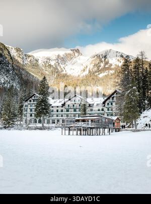 Hotel Lago di Prags im Winterschnee, mit dem gefrorenen See im Vordergrund und den dramatischen Berggipfeln der Dolomiten im Hintergrund, c Stockfoto