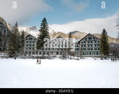 Hotel Lago di Prags im Winterschnee, mit dem gefrorenen See im Vordergrund und den dramatischen Berggipfeln der Dolomiten im Hintergrund, c Stockfoto