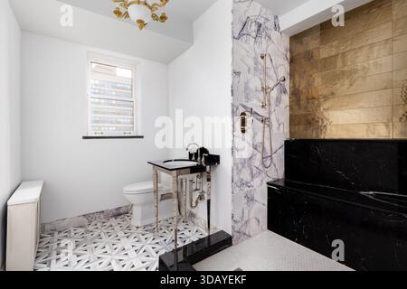 Ein luxuriöses, modernes Badezimmer mit eleganter schwarzer Duschbank, Wänden aus Calacatta-Marmor und Goldfliesen sowie Waschbecken und Kronleuchter in Gold. Stockfoto