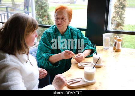 Eine ältere birassische Frau in einem gelben Oberteil lacht mit einer Afroamerikanerin zu Hause. Sie sitzen an einem Esstisch und unterhalten sich mit einem Tablet vor ihnen. Hohe Qualität Stockfoto