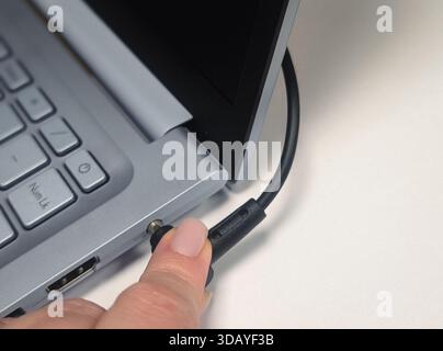 Nahaufnahme des Handsteckens des runden Ladekabels in den Netzanschluss des Laptops Stockfoto