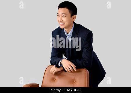 Träumender asiatischer Geschäftsmann, der sich auf Stuhl vor hellem Hintergrund lehnt Stockfoto