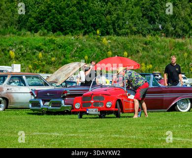 In einem großen Grasgebiet treffen sich die Menschen auf einer Oldtimer-Ausstellung, auf der Oldtimer ausgestellt werden. Die Teilnehmer bewundern die Fahrzeuge unter der Sonne und die Sozialisten Stockfoto