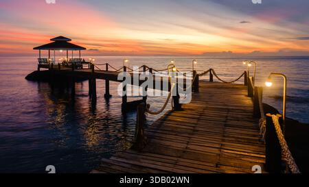 Ein wunderschöner Sonnenuntergang färbt den Himmel in leuchtenden Farben über dem ruhigen Wasser der Insel Koh Kood. Der hölzerne Pier erstreckt sich bis ins Meer und schafft eine friedliche Atmosphäre, die perfekt zum Entspannen in Thailand ist Stockfoto