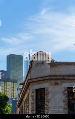 Die verwitterte Fassade eines alten Steingebäudes aus dem Jahr 1926 steht in starkem Kontrast zu hoch aufragenden modernen Glashochhäusern unter einem klaren blauen Himmel Stockfoto