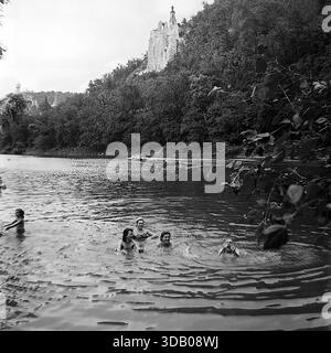 Slavyanogorsk (Svyatogorsk), Ukraine, UdSSR, 1950er Jahre Ein malerisches Schwarzweiß-Archiv, das die Sommerferien auf dem Seversky Donets River aufnimmt. Eine Gruppe glücklicher sowjetischer Leute schwimmt und badet im ruhigen Wasser. Im Hintergrund, die majestätischen Kreidefelsen und die historische St. Nikolaus Kirche der Heiligen Berge Lavra Turm über dem Fluss. Dieses stimmungsvolle Bild veranschaulicht anschaulich die Schönheit der Natur und den unbeschwerten Urlaub in der friedlichen Donbass-Region während der Sowjetzeit. Stockfoto