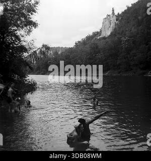 Slavyanogorsk (Svyatogorsk), Ukraine, UdSSR, 1950er Jahre Ein stimmungsvolles Schwarz-weiß-Archivfoto, das eine Sommerszene auf dem Seversky Donets River aufnimmt. Ein Paar schwimmt im Vordergrund; der Mann umarmt die Frau und zeigt in die Ferne, zeigt etwas. Im Hintergrund die majestätischen Kreidefelsen und der Turm der Nikolaikirche über dem Fluss. Dieses Bild veranschaulicht anschaulich romantische Freizeit und die landschaftliche Schönheit der „Donets Schweiz“ im friedlichen Donbass. Stockfoto