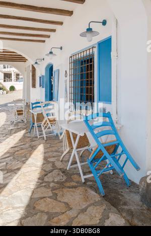 Sitzbereich im Freien eines traditionellen mediterranen Cafés unter einer Arkade, mit weißen Wänden, blauen Zierleisten, Holzstühlen und einer Steinterrasse Stockfoto