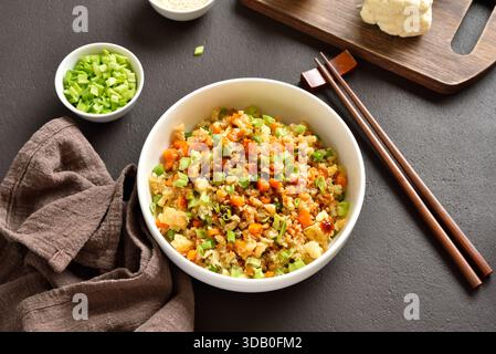 Blumenkohlreis im asiatischen Stil mit Karotten, grüner Erbse, Mais, Rührei in Schüssel auf dunkelbraunem Steinhintergrund. Stockfoto