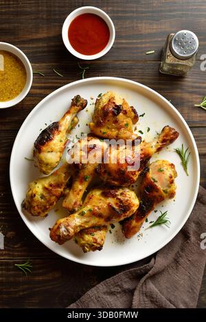 Barbecue mit gebratenen Hähnchenkeulen, serviert mit Sauce. Brauner Holzhintergrund, Draufsicht, flache Lage Stockfoto