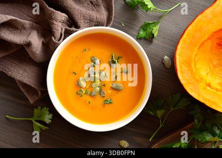Köstliche hausgemachte, cremige Kürbissuppe garniert mit Samen und Thymian auf braunem Holzhintergrund. Draufsicht, flach Stockfoto