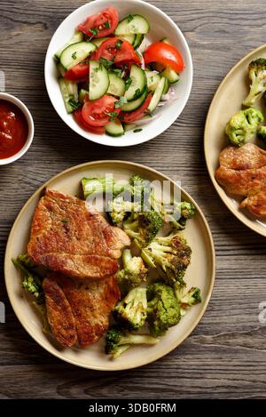 Gegrilltes Schweinefleisch, serviert mit gebratenem Brokkoli auf Teller auf braunem Holztisch. Draufsicht, flach Stockfoto