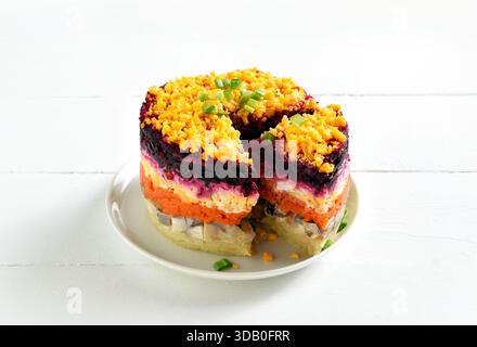 Mehrschichtiger Gemüsesalat mit Hering und gekochtem Gemüse auf weißem hölzernem Hintergrund. Nahansicht Stockfoto