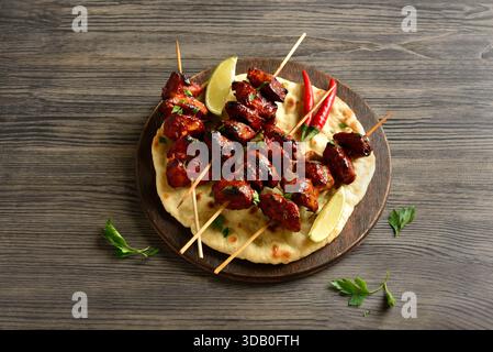 Tandoori Hähnchenspieße auf Fladenbrot auf Platte. Rustikaler Holzhintergrund, Nahansicht Stockfoto
